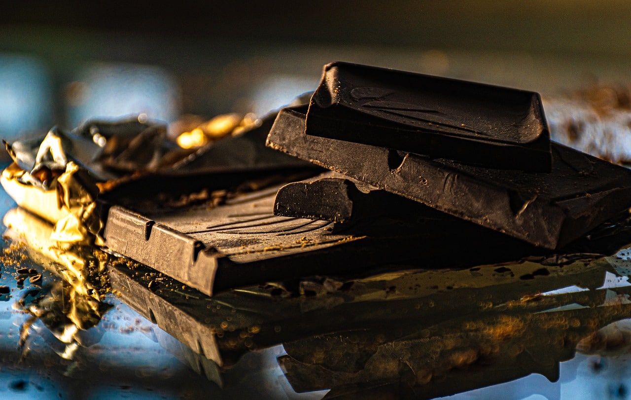 Close-up of premium dark chocolate bar partially unwrapped in golden foil, resting on a reflective surface